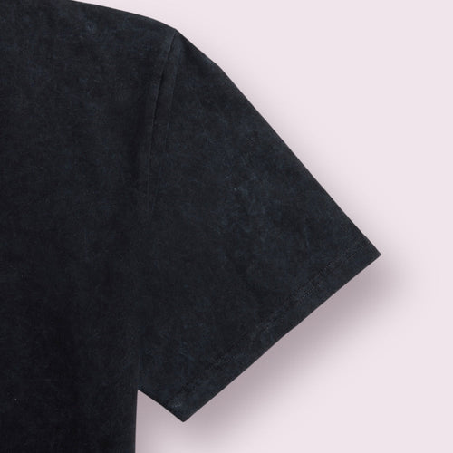 Close-up of a black short-sleeve t-shirt sleeve against a pale pink background.